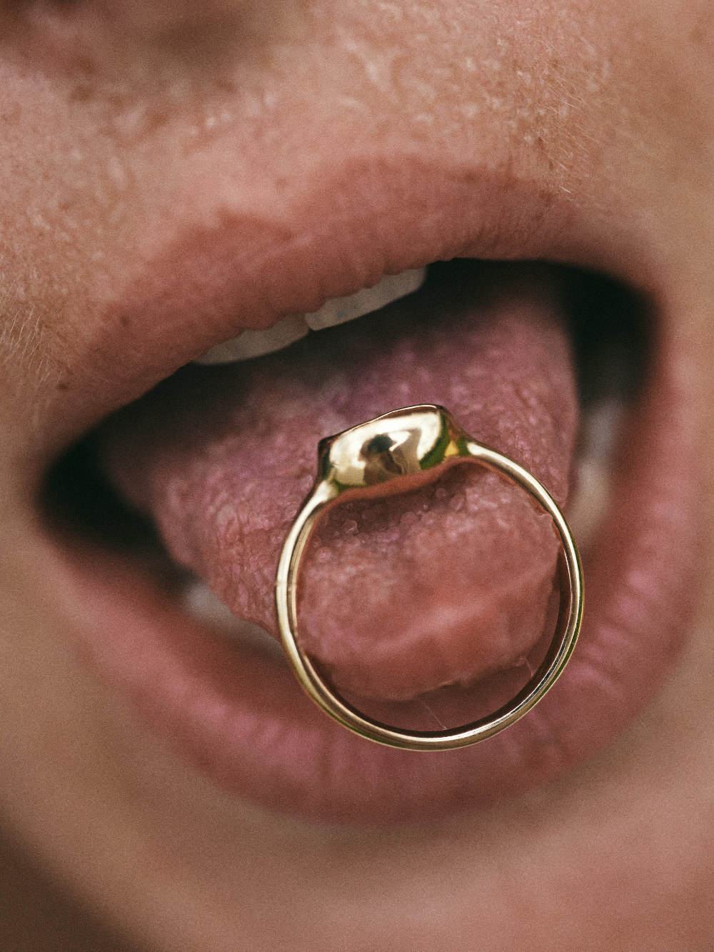 Carina Hardy fine yellow gold ring elegantly displayed on a model’s tongue. The roundness of the band with a unique and bold design of the piece.