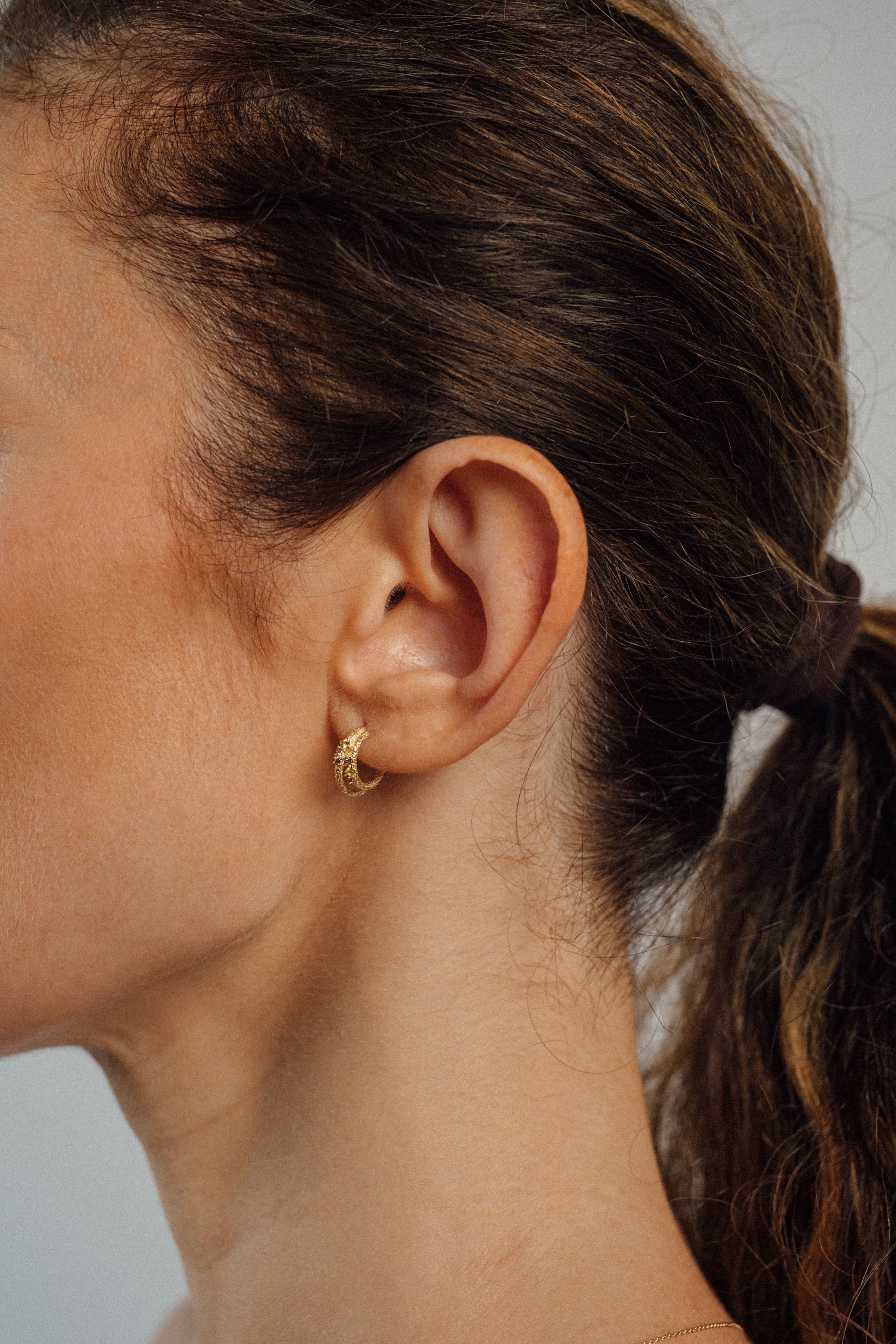Recycled 18K yellow gold crescent hoop earring that loops together below the lobe, pavé set with brown diamonds and yellow sapphires.