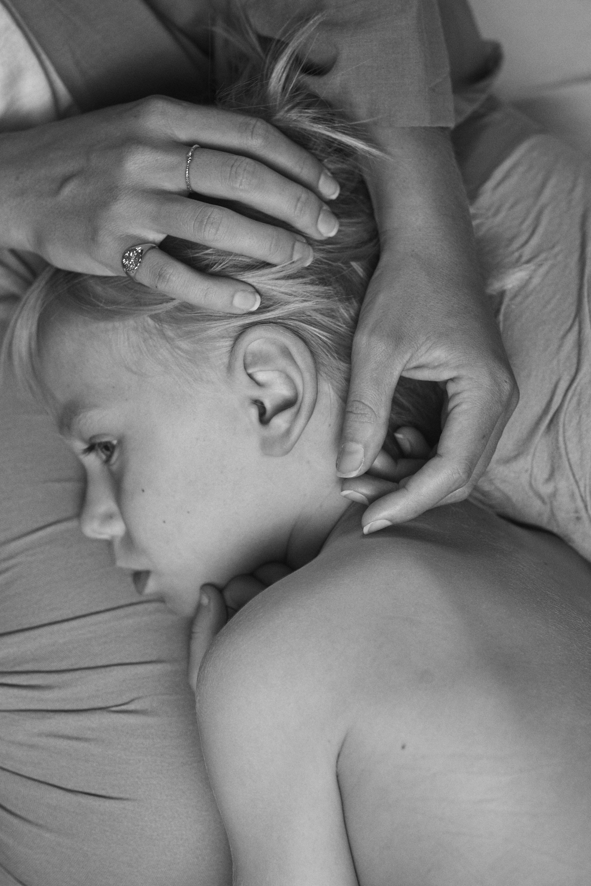 Peaceful black and white image of a child resting on their mother. Intimate moments embellished with Carina Hardy fine yellow gold jewelry. View the collection.