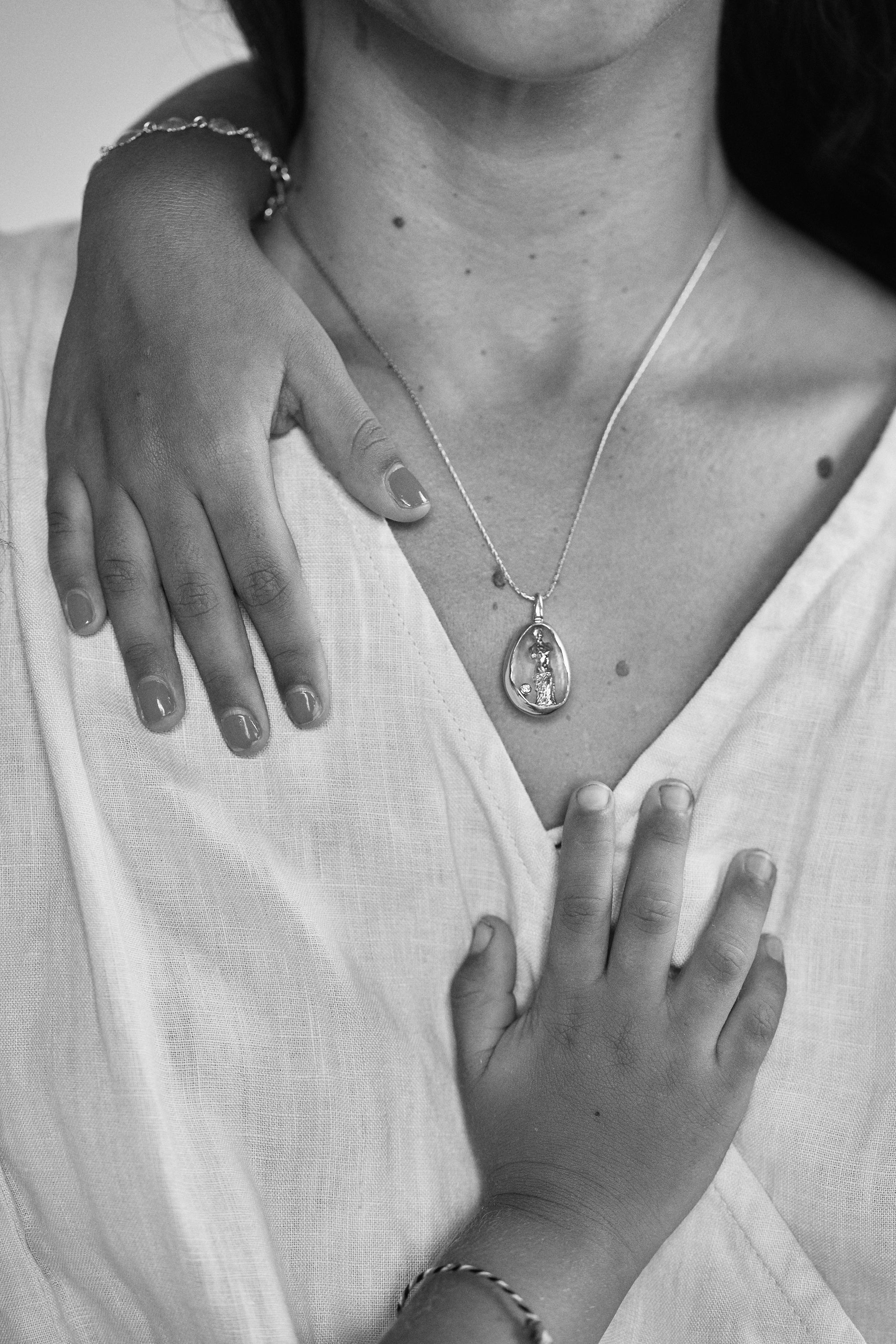 Black and white close-up of a woman and child, highlighting the Carina Hardy fine yellow gold Venus de Milo necklace. Beauty of connection, tender to the touch. View the collection.