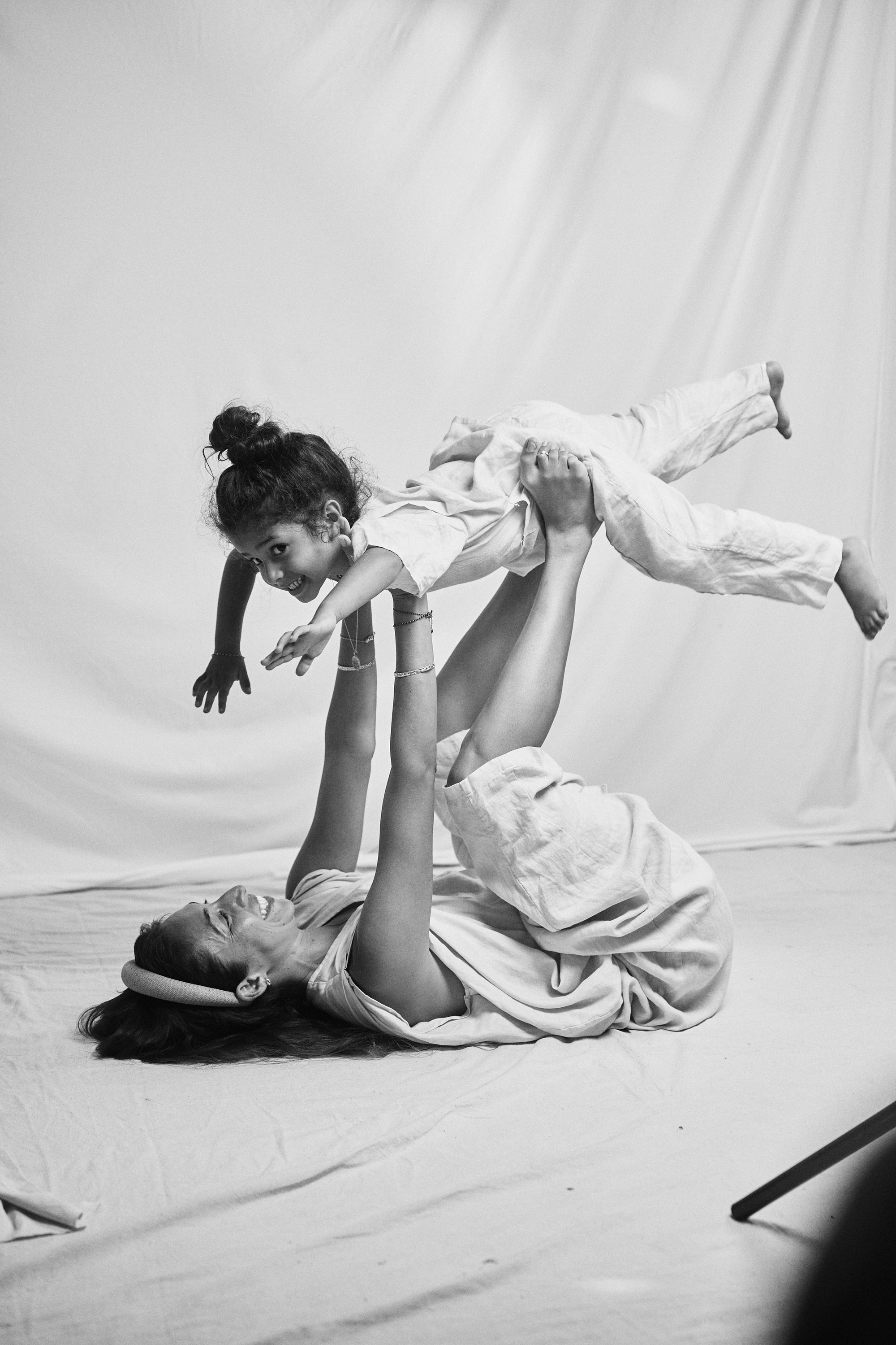 Heartwarming black and white capture of a mother playing with her child, suspended mid-air. Lasting memories and bond captured, embellished with Carina Hardy fine yellow gold jewelry.