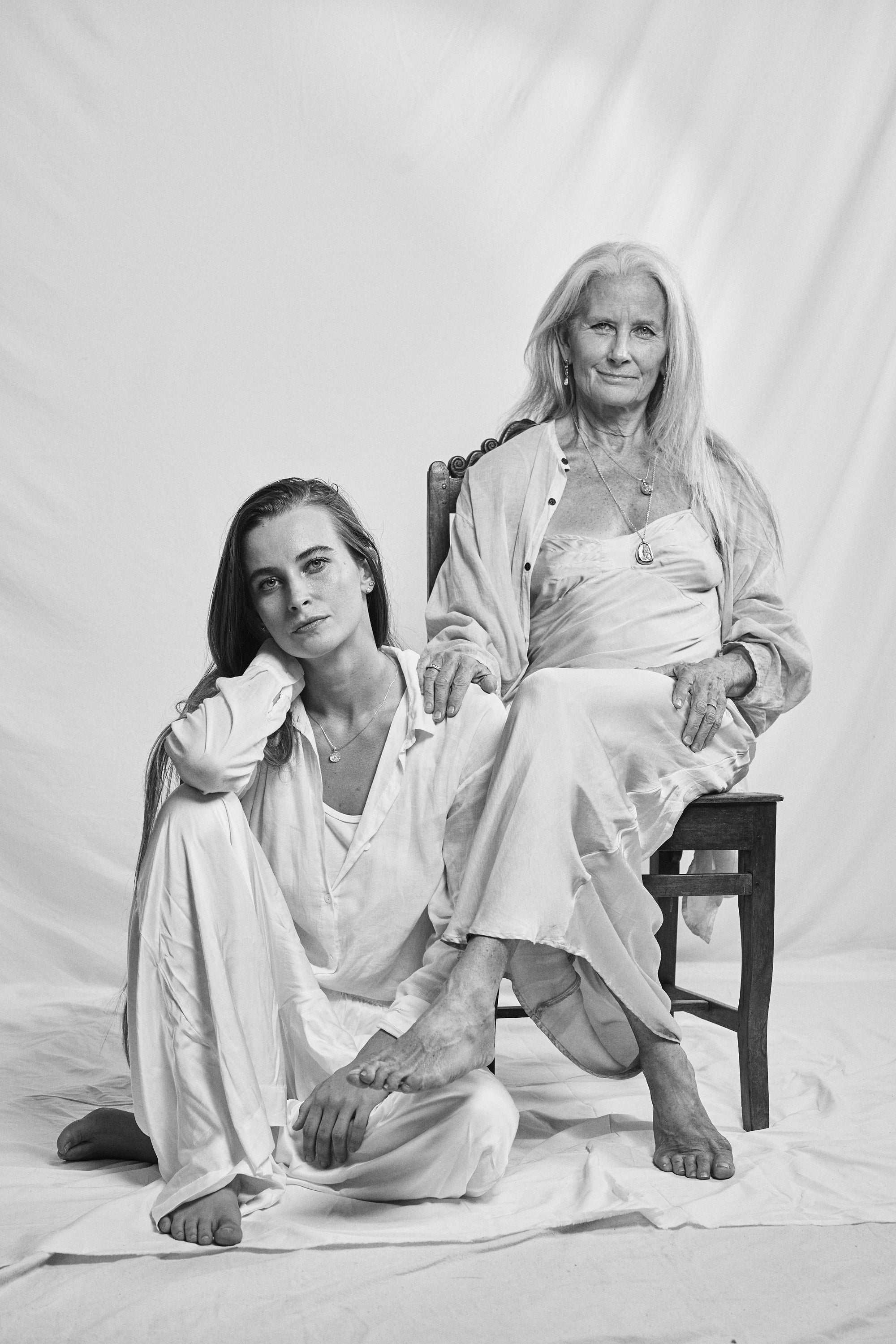 Black and white picture of a mother and daughter sitting together, mother on a chair and daughter beside her. Showcasing Carina Hardy Mother's Day fine yellow gold jewelry collection.