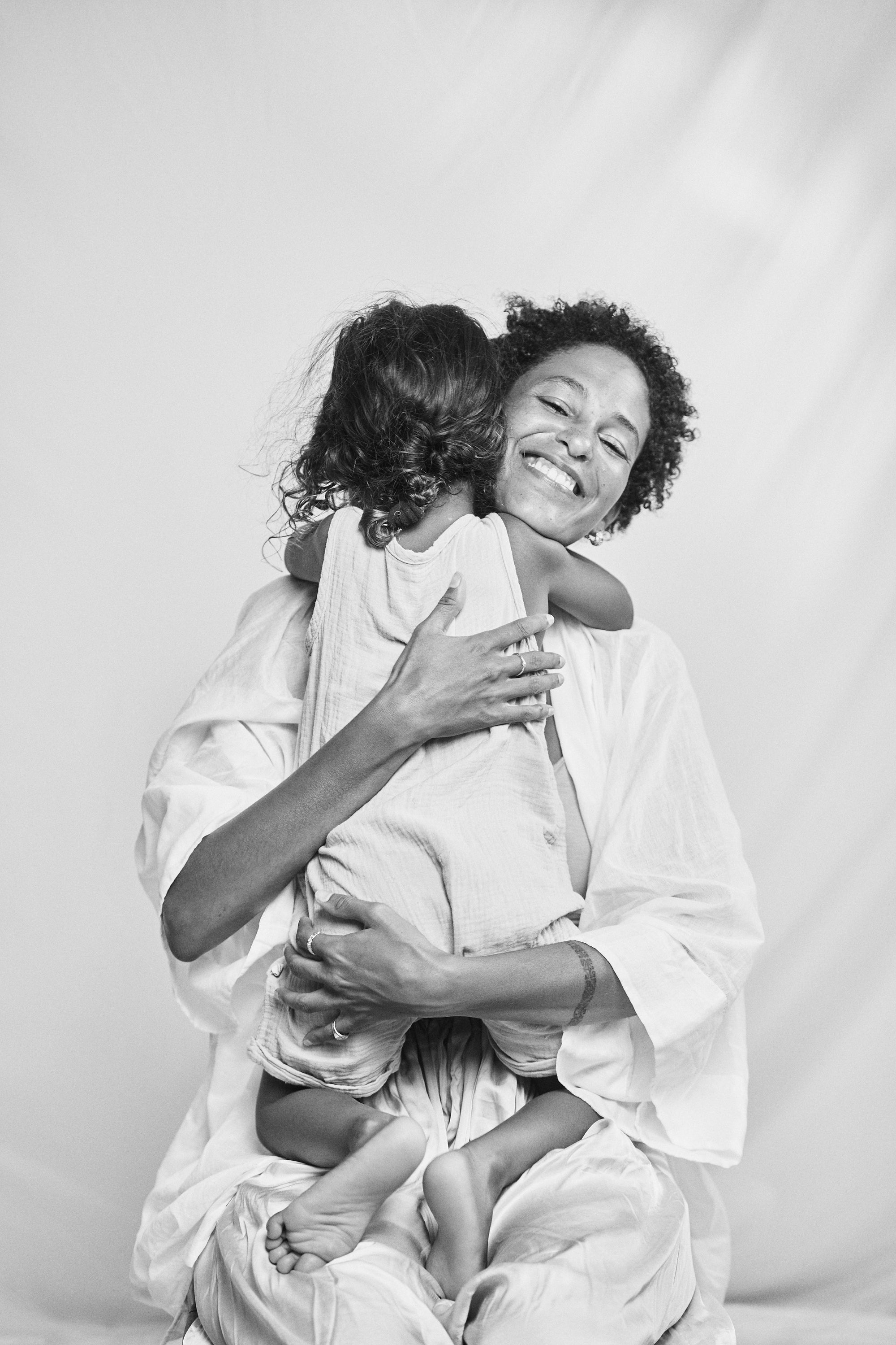 Black and white portrait of a mother and daughter embracing, both adorned with Carina Hardy fine yellow gold jewelry. Their love and elegance highlighted. View the collection today.