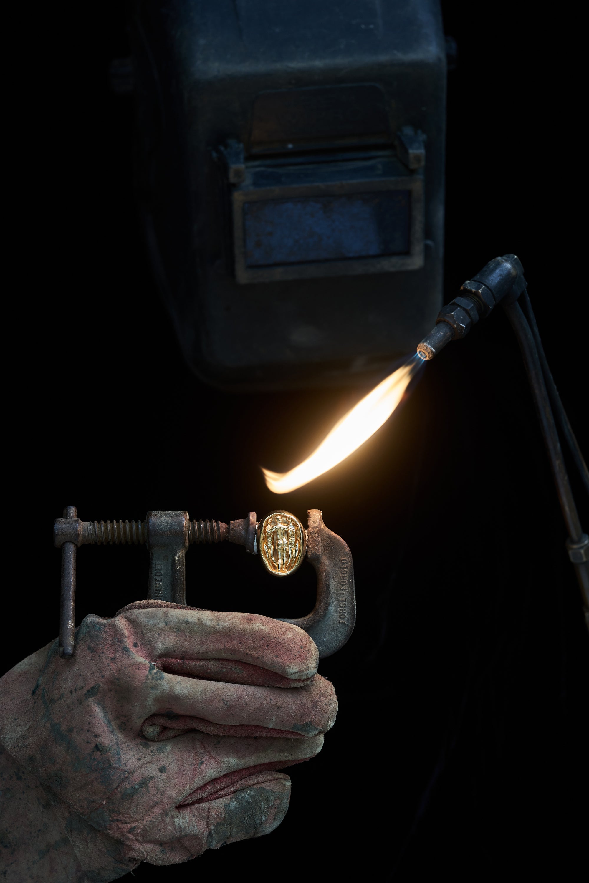 Jeweler using a torch to craft a piece of Carina Hardy fine yellow gold Roman Three Graces ring. The artisanal process and precision emphasized. View the collection today.