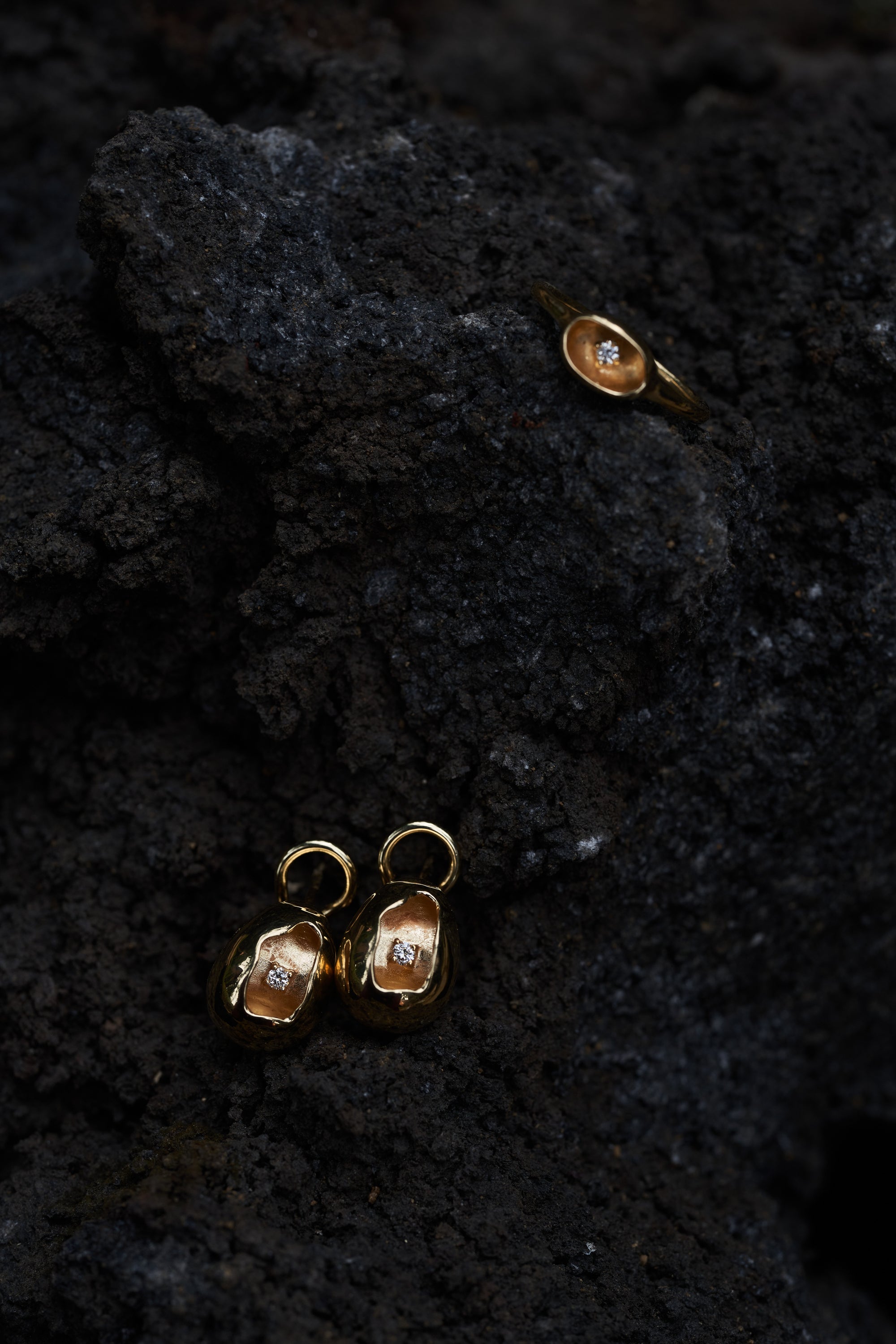 Close-up of Carina Hardy fine yellow gold jewelry featuring shiny diamonds arranged on a dark, textured surface, showcasing their intricate details and craftsmanship. View the collection today.