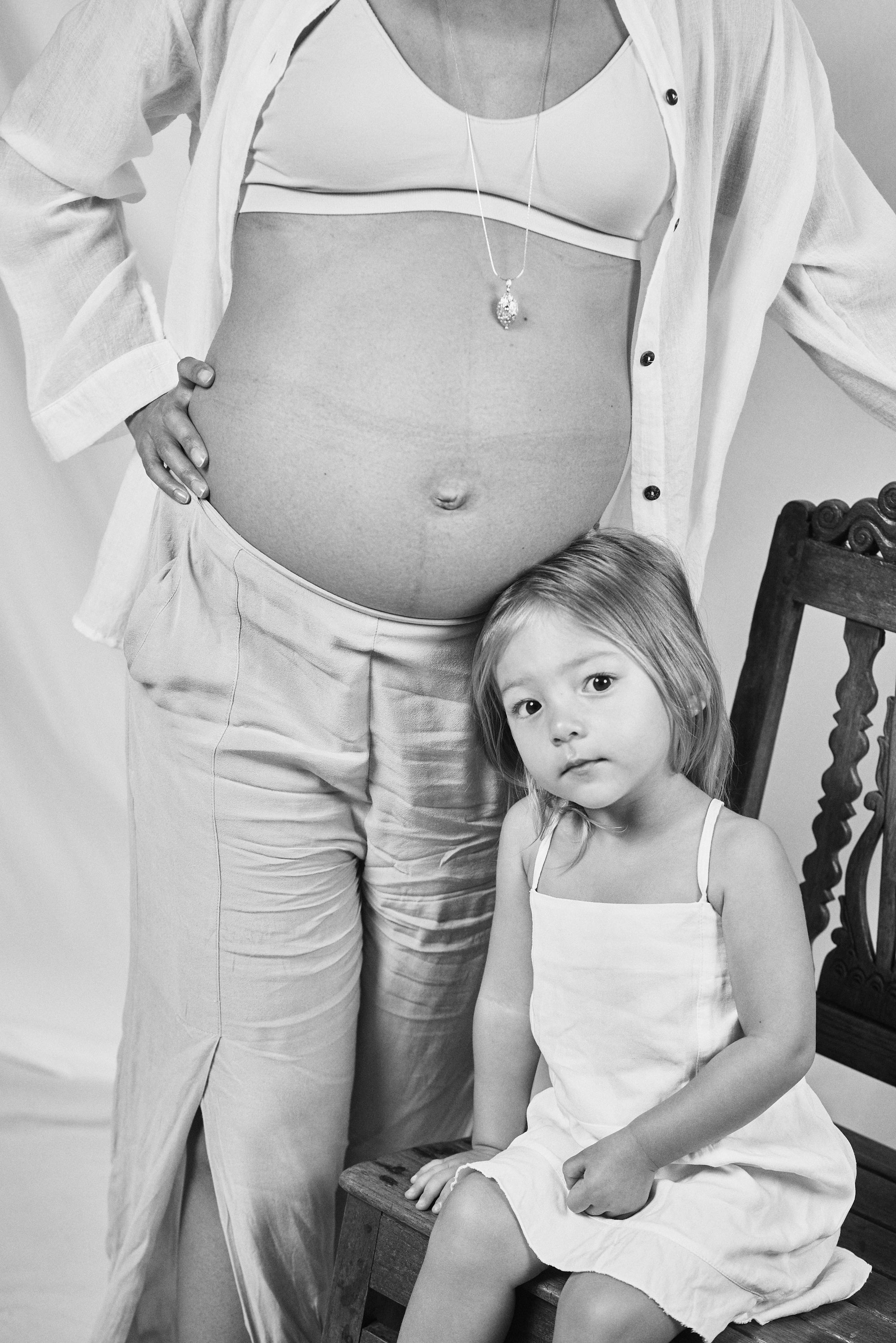 Black and white photo of a pregnant woman and her young daughter, both wearing Carina Hardy fine yellow gold jewelry. Present in life’s precious moments. View the collection.