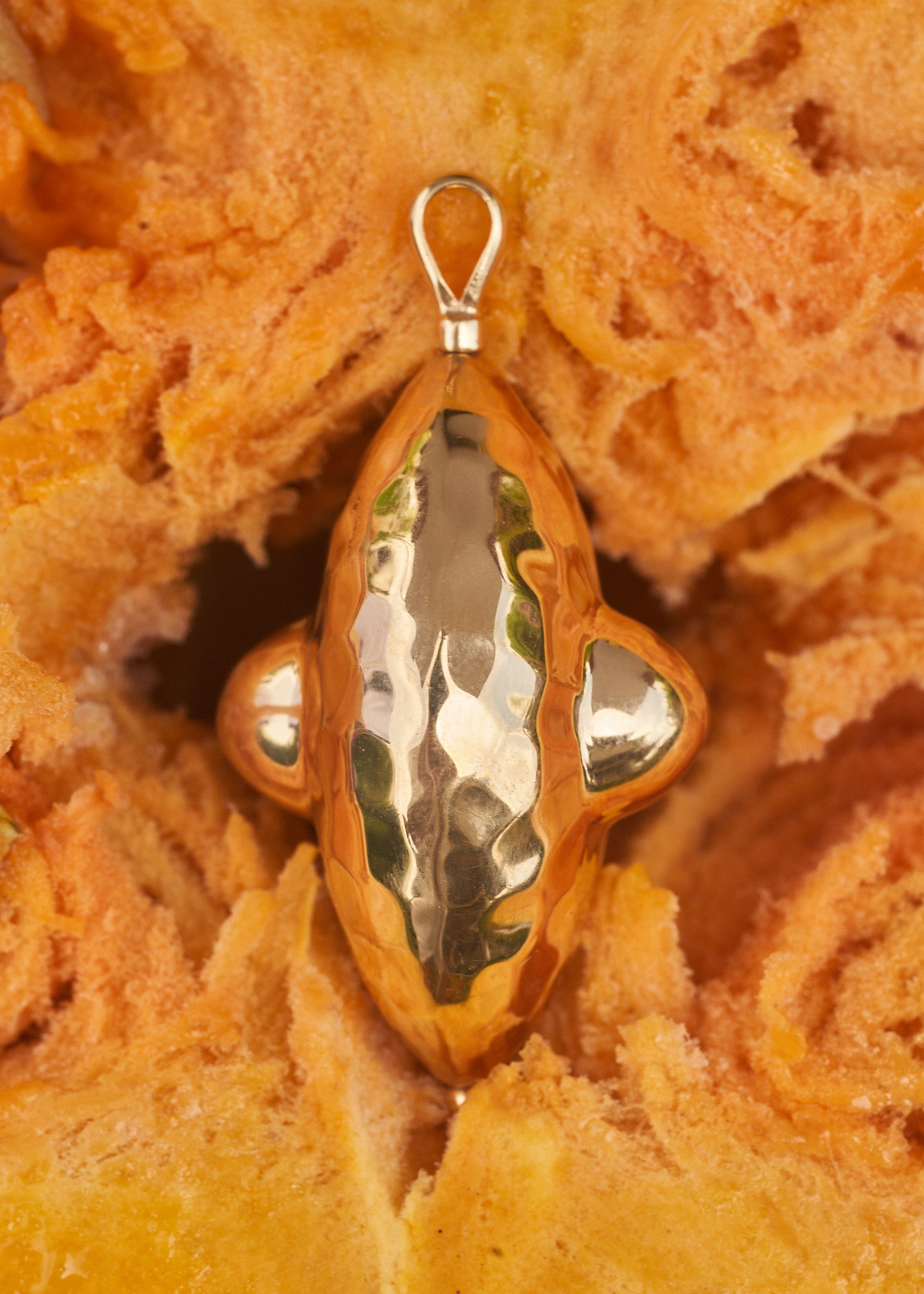 Close-up of a Carina Hardy fine sterling silver gold plated signature Elppin shape spinning pendant against an orange pumpkin background. Unique and exquisite craftsmanship. View the collection today.