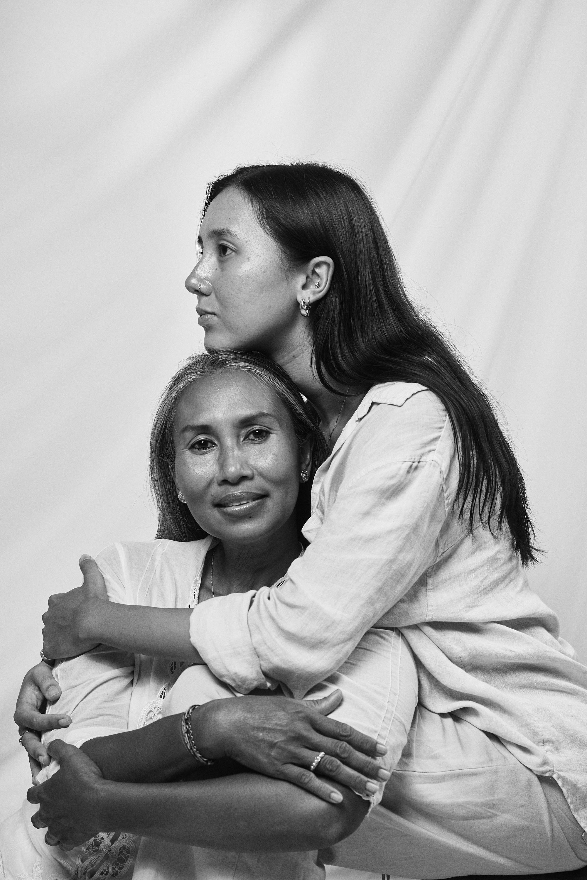 Black and white portrait of a mother embracing her daughter, both wearing Carina Hardy fine yellow gold jewelry. Warmth and elegance, view the collection today.