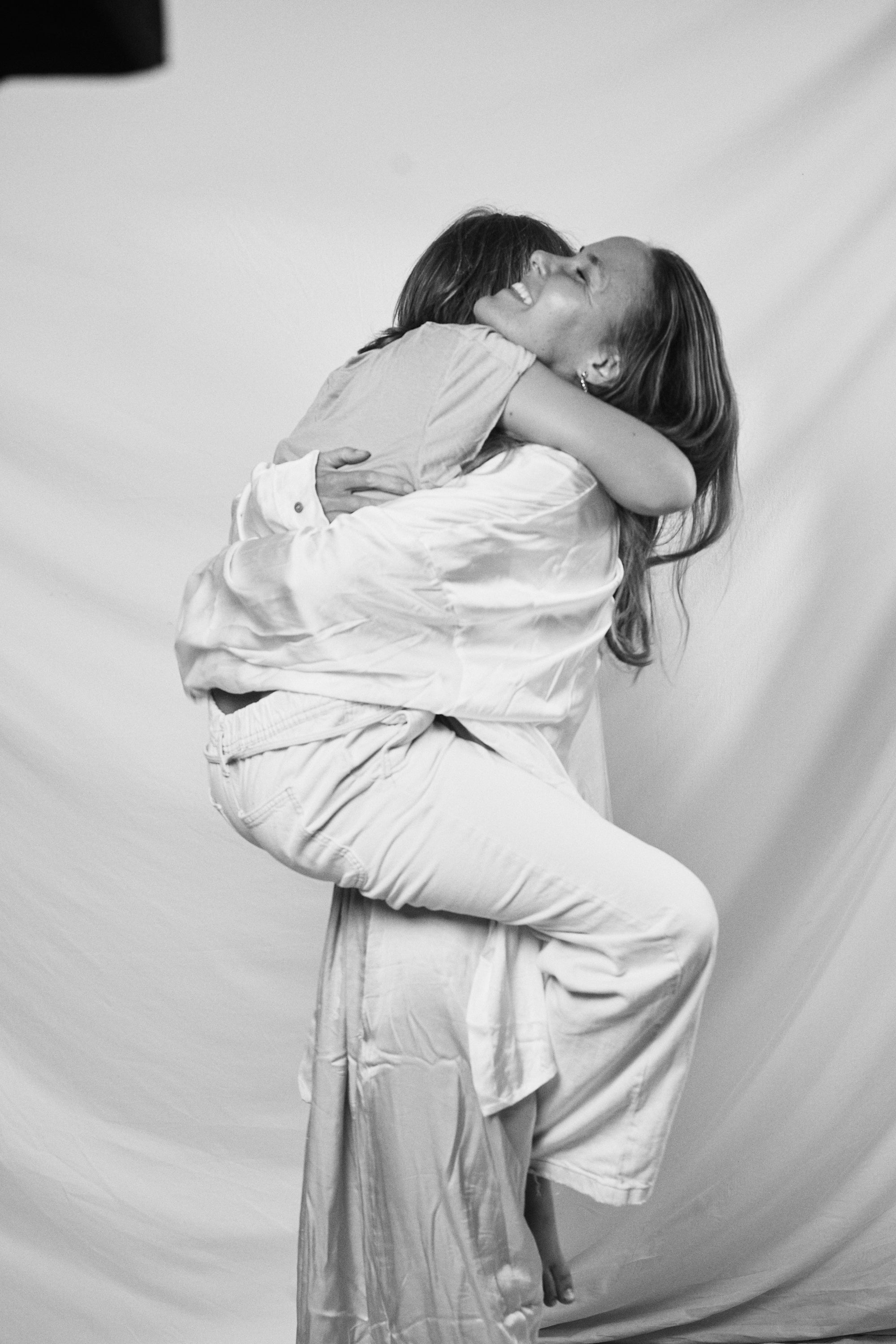 Black and white moment of a mother lifting her child, both wearing Carina Hardy fine yellow gold jewelry. View the collection.