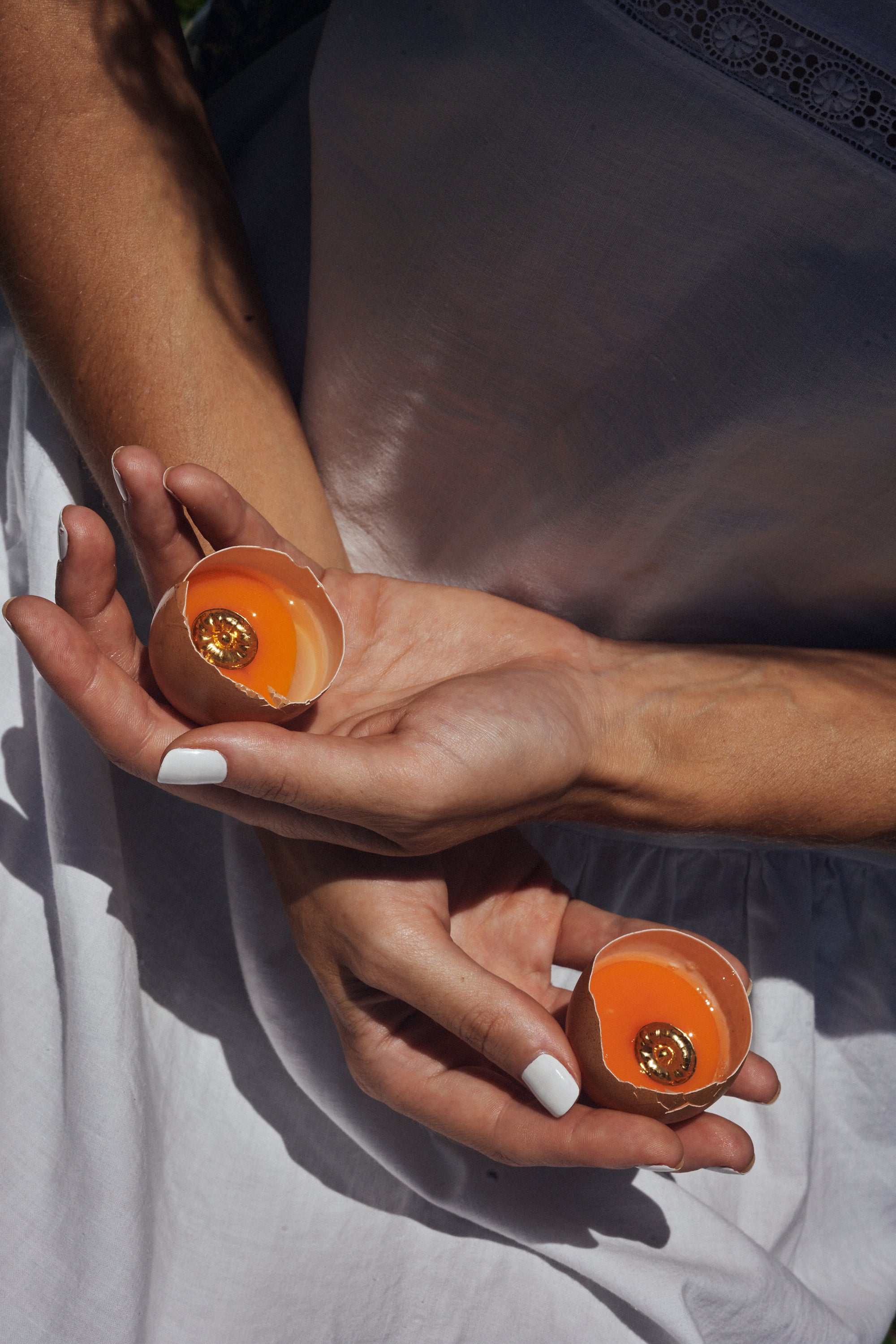 Carina Hardy fine sterling silver 22k gold plated round earrings encased in egg yolks on a model’s hands. The orange elements, showcases the luxury and unique design of the pieces.