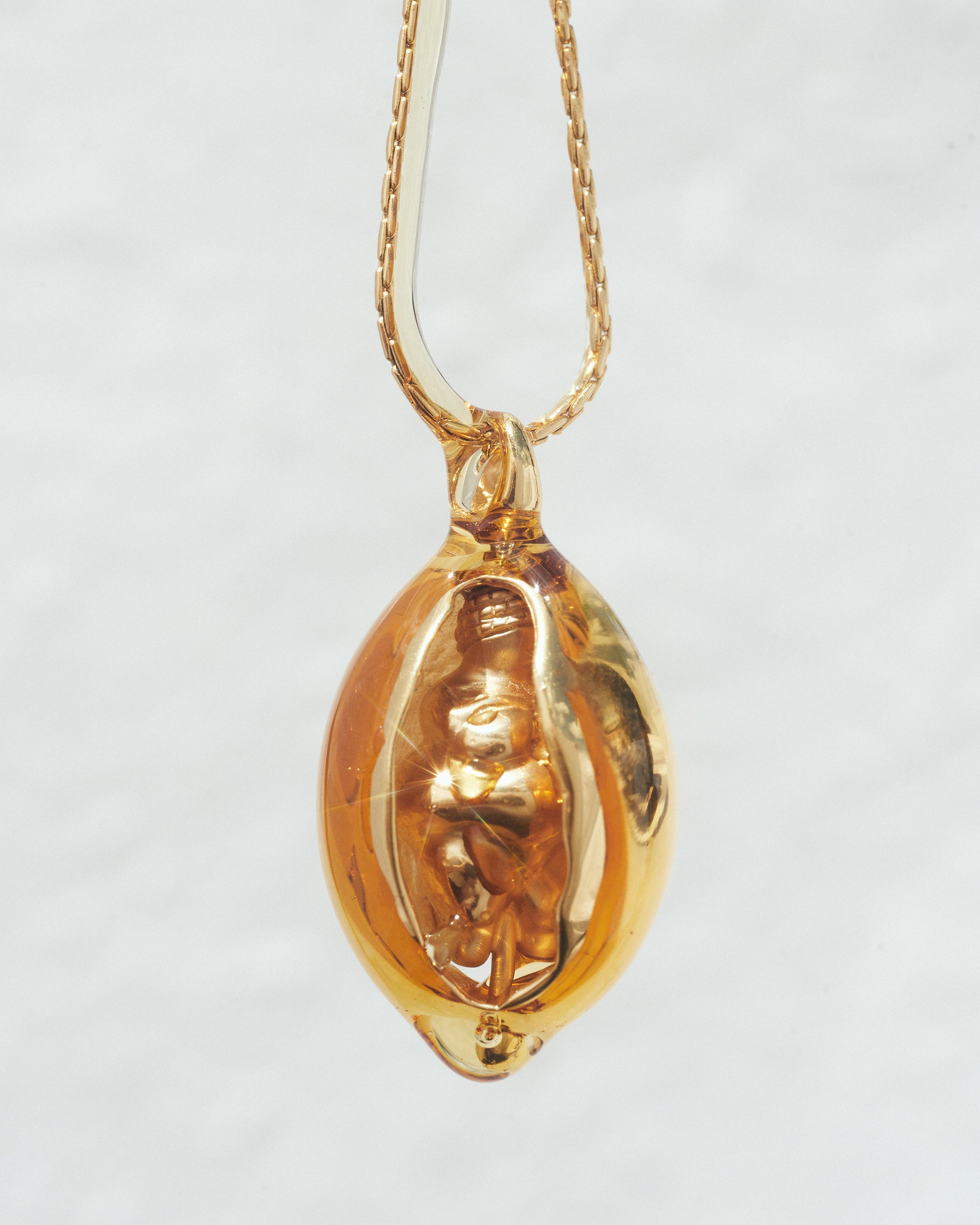 Close-up of a Carina Hardy fine yellow gold Woman of Willendorf necklace encased in honey. Dripping ever so slightly.