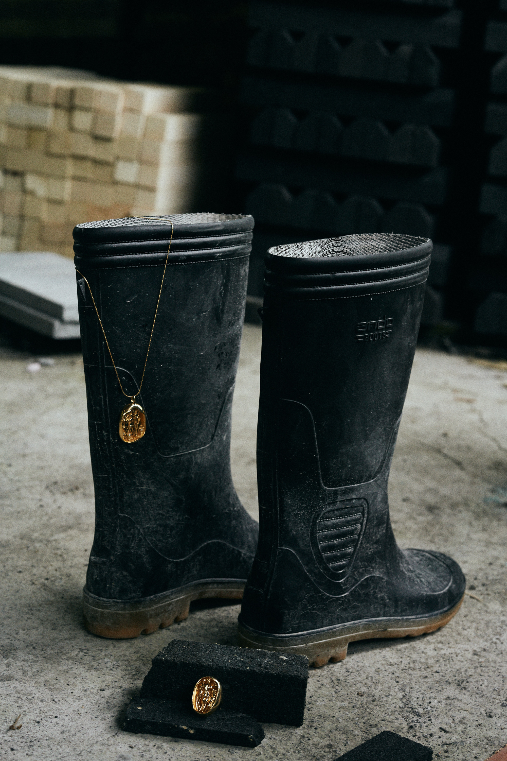 Carina Hardy fine yeloow gold jewelry pieces, including a necklace and ring, displayed creatively with a pair of black boots. The unique blend of elegance and rugged style highlighted. View the collection today.